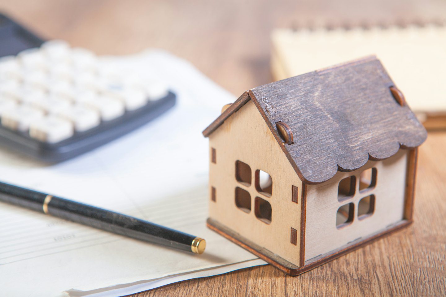 Casa de madera en miniatura sobre un escritorio de madera con material de oficina.