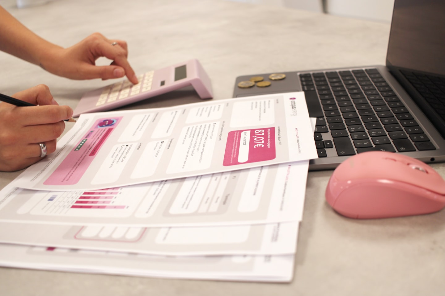 Persona revisando documentos financieros con calculadora rosa y portátil.